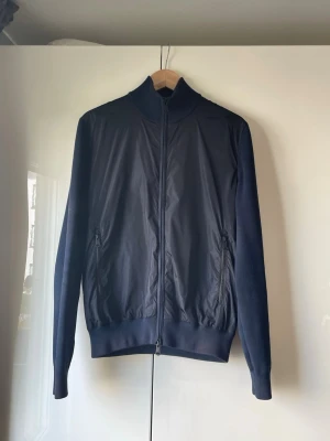 J.Lindeberg Cardigan  - Säljer en stilren marinblå cardiganjacka från J.Lindeberg. Storlek: S⭐️ Skick: 8/10 skick🌟 Nypris runt 2900 och mitt pris endast 1200! Hör gärna av dig vid frågor eller funderingar! Priset kan diskuteras vid en snabb och smidig affär. Modellnamnet är: Mack Hybrid Knit. 