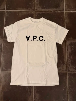 Vit t-shirt med svart A.P.C.-tryck - Säljer en vit t-shirt med svart A.P.C.-logga tryckt över bröstet. Klassisk rund halsringning och korta ärmar. Perfekt basplagg med stilren design som passar till det mesta.