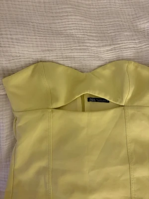 Gul axelbandslös kort klänning Zara - Trendig gul axelbandslös kort klänning från Zara. Klänningen har en snygg, figurnära passform och är tillverkad i ett slätt material som ger en stilren look. Perfekt för dig som vill sticka ut med en färgglad och modern outfit.
