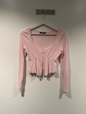 Ljusrosa croppad långärmad topp - Söt ljusrosa långärmad topp från Gina Tricot i storlek S. Modellen har spetsdetaljer, en liten rosett framtill och en lätt volangkant längst ner. Mjukt och stretchigt material som sitter fint på.  ✨ Skick: Bra begagnat skick, inga synliga hål eller fläckar. 📏 Storlek: S 🏷️ Märke: Gina Tricot 🎀 Färg: Ljusrosa  Perfekt till jeans, kjol eller lågmidjade byxor för en feminin och trendig look.
