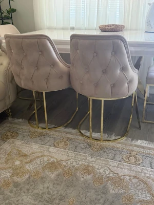 Beige sammetsstolar med guldfärgade ben - Fyra leganta stolar i beige sammet med mjukt vadderad sits och ryggstöd. Stolarna har dekorativa knappar och stilrena guldfärgade metallben i modern design. Perfekta som matbordsstolar eller accentstolar i vardagsrummet.