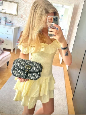 Gul volangklänning med offshoulder - Helt ny, gul kortklänning med volanger och offshoulder-design. Klänningen har smockad överdel och flera lager i kjolen för en luftig känsla. Perfekt för sommarens varma dagar och har en romantisk look. Med prislapp
