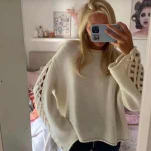 Vit oversized stickad tröja - Säljer en vit oversized stickad tröja med breda ärmar och dekorativa håldetaljer längs ärmarna. Tröjan har rund halsringning och är gjord i ett mjukt, tjockt material som ger en avslappnad look. Perfekt för dig som gillar trendiga och bekväma plagg. Storlek s💓