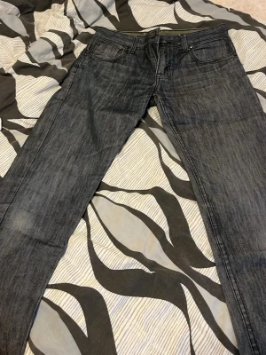 Grå Levi's jeans med raka ben - Säljer ett par grå jeans från Levi's med klassisk femficksmodell och raka ben. Jeansen har en diskret tvättad look och detaljer som den röda Levi's-lappen på bakfickan samt svart patch bak i midjan. Perfekta för en avslappnad och stilren outfit.
