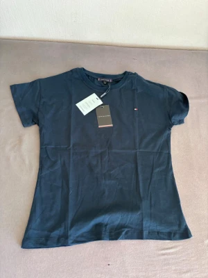 Mörkblå t-shirt från Tommy Hilfiger - Snygg mörkblå t-shirt från Tommy Hilfiger med liten logga på bröstet. Klassisk passform och rund halsringning. Tillverkad i mjuk bomull som känns skön mot huden. Perfekt till jeans eller shorts för en clean look.
