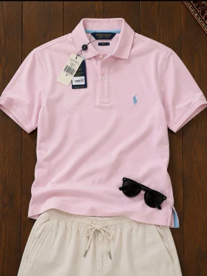 Ljusrosa pikétröja från Ralph Lauren - Snygg ljusrosa pikétröja från Polo Golf Ralph Lauren med klassisk krage och korta ärmar. Tröjan har blå broderad logga på bröstet och knäppning vid halsen. Perfekt för en stilren och avslappnad look.