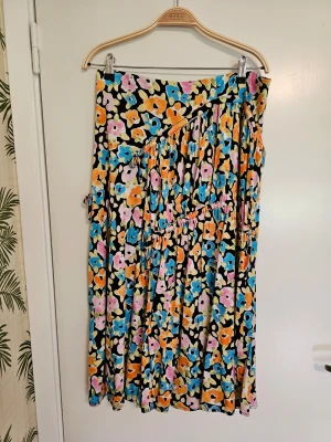 Midikjol Paloma från Stine Goya - Midikjolmed blommigt mönster i blått, orange, rosa, gult och svart. Kjolen har en avslappnad passform och är tillverkad i mjuk viskosjersey som ger ett snyggt fall. Effektfulla knytband som gör att kjolens vidd kan anpassas.