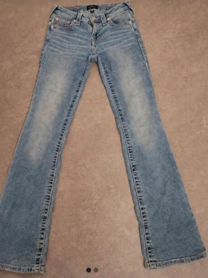 Ljusblå bootcut jeans med brodyr - Säljer ett par ljusblå bootcut jeans med snygg slitning framtill och broderade detaljer i rosa och vitt på bakfickorna. Jeansen har klassisk femficksmodell och är tillverkade i denim. Perfekta för dig som gillar en retrostil! Byxorna är aldrig använda och är samma bilder som min vinted "Aliceesellout", storlek w25