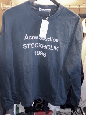 Longsleeve Acne Studios - Cool blå långärmad topp från Acne Studios med tryck 'STOCKHOLM 1996' framtill. Klassisk rund halsringning och relaxed fit. Perfekt till jeans eller kjol för en clean och trendig look.