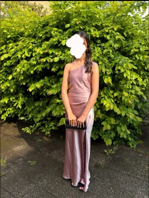 Ljusrosa långklänning i satin - Använd 2ggr, den kostar över 1000kr ny. Jag är ca 1,65 men passar något kortare& längre. Elegant ljusrosa långklänning i satin med oneshoulder-design och hög slits framtill. Klänningen har en figurnära passform och markerad midja som ger en snygg siluett. Perfekt för speciella tillfällen. (Den är skrynklig på bilden för att jag inte hann fixa, men är superlätt att göra slät)