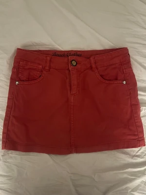 Röd jeanskjol - Snygg röd jeanskjol med fem fickor och knapp framtill. Kjolen har bälteshällor och klassisk jeanskjolsdesign. Snygg och unik till sommaren! Använd ett fåtal gånger!