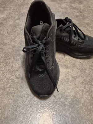 Svarta sneakers från alo - Stilrena svarta sneakers från alo med tjock sula och diskreta detaljer. Skorna har snörning och är tillverkade i textilmaterial med syntetdetaljer. Perfekta för en sportig och modern look.