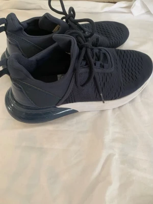 Mörkblå sneakers med vit sula - Snygga mörkblå sneakers med ventilerande mesh-ovandel och vita sulor. Skorna har snörning och en stabil hälkappa i plast för extra support. Perfekta för dig som vill ha en sportig och modern look till vardags. Passar till det mesta och är riktigt bekväma. Köpta för 200kr. Använda max 5 gånger