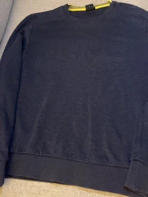 Mörkblå sweatshirt från Hugo Boss - Snygg mörkblå sweatshirt från Hugo Boss med diskret broderad logga på bröstet. Tröjan har rund halsringning, ribbade muddar vid ärmslut och nederkant samt en klassisk passform. Perfekt för en stilren och avslappnad look.