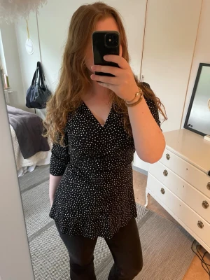 Svart prickig omlottopp - Snygg svart omlottopp med vita prickar. Knappt använd och i mycket bra skick, då det går att knyta den i ryggen så passar storleken många! 💓 hör gärna av dig vid frågor!