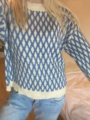 Blåvit stickad tröja med mönster - Mysig stickad tröja i blått och vitt med ett upprepat mönster över hela plagget. Tröjan har rund halsringning och ribbade muddar vid ärmslut och nederkant. Perfekt för dig som gillar en avslappnad och trendig stil. (Vet ej vilket märke)