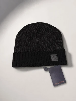 Svart mössa med rutig mönster - Snygg svart mössa med rutigt fint mönster och med diskret logopatch framtill och ribbad uppvikt kant. Tillverkad i ett mjukt, stickat material som känns lyxigt och stilrent. Perfekt accessoar för dig som vill ha en exklusiv touch på din outfit.