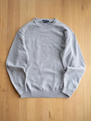 Grey Crew Neck, size XL - Ljusgrå stickad tröja från McNeal i klassisk modell med rund halsringning och ribbade muddar vid ärmslut och nederkant. Tröjan är enkel och stilren, perfekt för lager på lager och passar till det mesta. Materialet ser ut att vara mjukt och bekvämt.