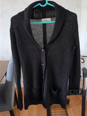 Svart stickad kofta Ralph Lauren - Svart stickad kofta från Denim & Supply Ralph Lauren med två fickor framtill och stora knappar. Koftan har en bred sjalkrage och är tillverkad i ett luftigt, grovstickat material. Perfekt att slänga över en t-shirt för en avslappnad look.