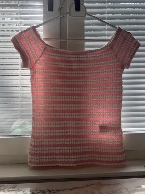 Topp - Söt stickad topp med rosa och vita ränder. Modellen har korta ärmar och en bred, rundad halsringning. Materialet ser mjukt och stretchigt ut, perfekt för en avslappnad och trendig look. Passar bra till jeans eller kjol.