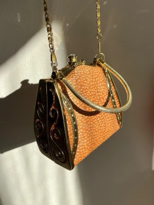 Vintage orange kuvertväska med metall - Unik aftonväska i korallfärg med strukturmönster och detaljer i guldmetall. Väskan har både lång kedja som är avtagbar och handtag i metall samt dekorativa sidor med snirkliga mönster. Stängs med ett klassiskt metallspänne och har en elegant, retro känsla. #katespade 