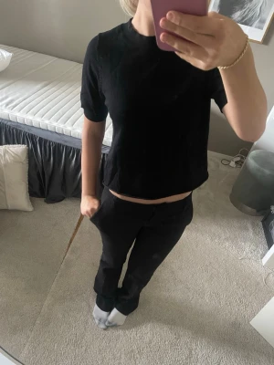 Svart croppad t-shirt - En enkel svart croppad t-shirt med rund hals och korta ärmar. Passformen är normal och toppen är perfekt för en clean och stilren look. Materialet ser ut att vara bomull eller en bomullsblandning. Som ny 