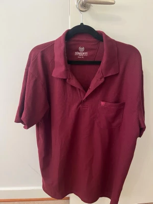 Vinröd pikétröja Simenti Classic med bröstficka - Strl XL (passar L) - Stilren vinröd / mörkröd pikétröja från Simenti Classic med en snygg våffel-/piquéstruktur. Försedd med bröstficka och en diskret broderad logotyp. Märkt som XL, men upplevs passa bäst som en Large (L).  Skick: Mycket fint skick, hel och ren.  Färg: Vinröd / Burgunder  Detaljer: Bröstficka med brodyr, texturerat tyg  Storlek: Märkt XL (passar som L)  Märke: Simenti ✨ Kika gärna på mina andra varor på sidan! Jag säljer just nu av en stor del av garderoben med allt från märkeskläder och rejäla jac