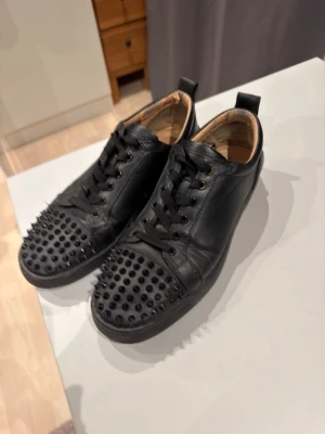 Svarta sneakers med nitar - Säljer ett par svarta sneakers i läder med coola svarta nitar över tån. Skorna har svarta skosnören och en låg profil. Insidan är beige och de har en klassisk rund tå. Perfekta för dig som vill sticka ut med din stil. Lite skitiga men inga problem. Går att pruta