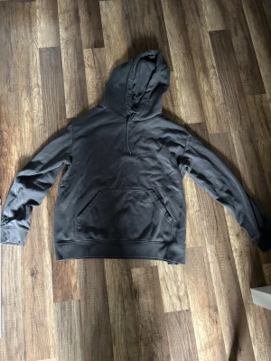 Mörkgrå hoodie från H&M - En enkel och stilren mörkgrå hoodie från H&M med huva och känguruficka framtill. Tillverkad i mjukt bomullsmaterial och har ribbade muddar vid ärmslut och nederkant. Perfekt för en avslappnad och bekväm look. Oversize onesize
