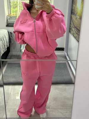Oversized rosa loungewear set - Säljer ett oversized loungewear set i starkt rosa färg. Setet består av en zip-hoodie med hög krage och broderad detalj på bröstet samt matchande byxor med resår i midjan och broderad detalj på benet. Mjukt material, perfekt för chill dagar hemma.