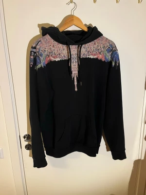 Marcelo Burlon hoodie - Säljer en svart hoodie från Marcelo Burlon. Den är använd men fortfarande i bra skick förutom ett lite hål vid fickan som ni ser på sista bilden. Storlek S.