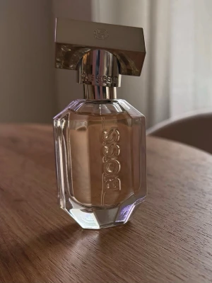 BOSS The Scent Eau de Parfum for Women 30 ml. - BOSS The Scent For Her Eau de Parfum – 30 ml  Varm, feminin och sensuell doft med mjuk fruktig sötma. 🍑✨ Doften öppnar med persika och fresia, följt av osmanthus och avslutas med rostad kakao, som ger en varm och lätt gourmandaktig karaktär.  Ca 85-90 % kvar – se bilder för aktuell nivå. Säljs utan originalkartong.