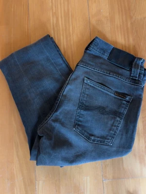 Mörkgrå smala jeans från Nudie - Säljer ett par mörkgrå jeans från Nudie med smal passform och klassisk femficksdesign. W30, L32. Hör av er vid funderingar.