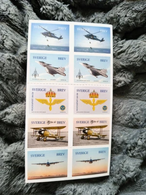 Frimärken Flygvapnet 100 år Sverige - Ett ark med 10 svenska frimärken från PostNord med motiv av flygplan och symboler från Flygvapnet, utgivna för att fira Flygvapnet 100 år. Frimärkena har olika färger och illustrationer av både moderna och äldre flygplan samt emblem.