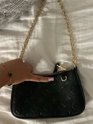 Svart axelremsväska med kedja - Snygg svart handväska i präglat läder med klassiskt monogrammönster och guldfärgad kedjerem. Jättefint skick. Dm för med bilder 