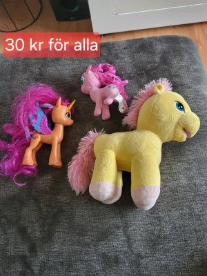 Tre färgglada ponyleksaker - Säljer ett set med tre ponyleksaker: en gul mjukisponny med rosa man och svans, en rosa plastponny med lila man och en orange plastponny med lila vingar, horn och rosa man. Perfekt för dig som gillar fantasifulla leksaker och vill ha något unikt till samlingen. Där e 2 små fläckar på den gula som man kan se på bilderna.