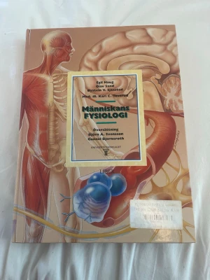 Människans fysiologi kursbok - Kurslitteratur i fysiologi med detaljerade illustrationer av människokroppen. Boken har ett beige omslag med anatomiska bilder och tydlig titel på framsidan. Skriven av Egil Haug, Olav Sand, Øystein V. Sjaastad och Karl C. Toverud. Utgiven av Liber och Universitetsforlaget.