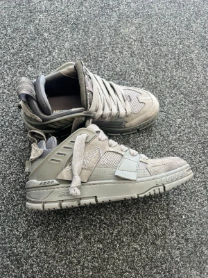  Arigato skor - Snygga grå sneakers från Arigato med chunky sula och breda skosnören. Ovandelen är i mesh och mocka med detaljer i läder och textil. Märkeslogga på sidan och tungan. Perfekta för dig som gillar streetwear och modern stil. Pris kan förhandlas