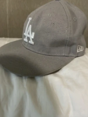 Grå LA-keps från New Era - Snygg grå keps från New Era med LA-logga broderad i vitt framtill. Klassisk modell med böjd skärm och ventilerande hål upptill. Tillverkad i slitstarkt tyg och har MLB-logga baktill. Perfekt för dig som gillar streetwear och sportig stil.