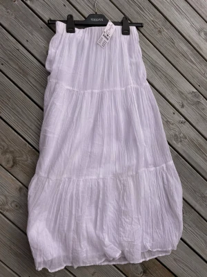 Vit långkjol från Gina Tricot - Luftig och lång vit kjol från Gina Tricot i storlek S. Kjolen har ett crinklat tyg och resår i midjan för en bekväm passform. Perfekt för en avslappnad och trendig look under varma dagar.