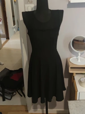 Vero Mods ärmlös klänning med rund hals - Säljer en svart klänning med rund hals och ärmlös design. Klänningen har en figurnära överdel och utställd kjol som ger en klassisk siluett. Perfekt för dig som gillar enkel och stilren look.