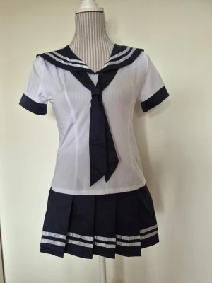 Japansk skoluniform cosplay set - Sailor set från WeisGirl.   Denna sjömansinspirerade outfit består av en kortärmad topp med en klassisk sjömanskrage och en matchande plisserad kjol. Toppen har en knuten slipsdetalj framtill och kjolen är designad med vita ränder längs nederkanten. En vit trosa med smala band medföljer också.  Storlek S men eftersom att kjolen är justerbar uppskattar jag att den kan passa XXS-S. Helt nytt med tags. 