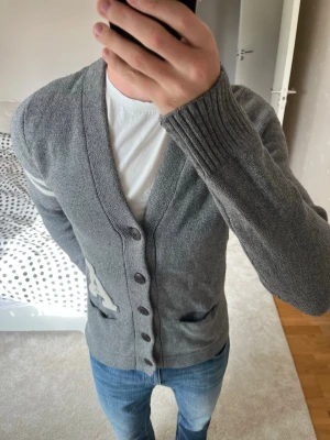 Grå kofta med knappar och fickor - Säljer en riktigt snygg grå stickad cardigan från Abercrombie&Fitch i väldigt fint skick utan defekter. Cardiganen är i storlek M! 😊✌🏼—————————————————————————————                                                     📐| Storlek: M                                                           👖| Märke: Abercrombie & Fitch                           🔎| Skick: Mycket fint skick                                                ✍🏻| Skriv om du har några frågor 