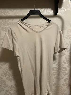 Vit basic t-shirt med v-ringning - En enkel vit t-shirt med v-ringad hals och korta ärmar. Tillverkad i mjukt bomullsmaterial som känns skönt mot huden. Perfekt till jeans eller shorts för en clean och avslappnad stil.