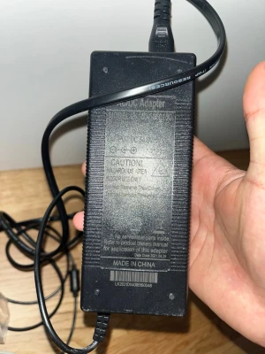 Svart nätadapter med 3-polig kontakt - Säljer en svart nätadapter med 3-polig rund kontakt. Adaptern har räfflade sidor för bättre grepp och tydlig märkning på framsidan. Passar till olika elektroniska enheter som kräver denna typ av strömadapter. Tillverkad i plast.