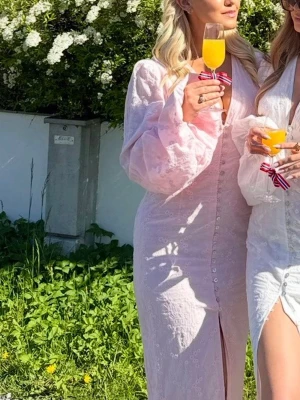Rosa adoore klänning - Positano maxiklänning från Adoore i rosa broderi. Klänningen har knappar och slitsar framtill, voluminösa långa ärmar samt en V-ringad krage. Livstycket är helt fodrat, har en dold dragkedja baktill och en hellång silhuett. Designad med en smalare midja för att framhäva figuren. Den är endast använd en gång på 17 maj i år i Norge, så den är i väldigt bra skick 🩷Kan ta betalning via Plick eller Swish ☺️