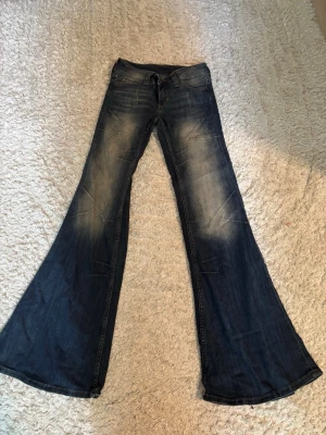 Mörkblå utsvängda jeans - Säljer ett par mörkblå jeans med kraftigt utsvängda ben och slitna detaljer framtill. Jeansen har klassisk femficksmodell och låg midja. Har bara använts en gång och är i helt nytt skick! Storlek 26/32