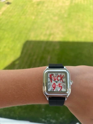 ”Fuck 9-5” klocka - Säljer en unik klocka med kvadratisk silverfärgad boett och svart silikonband. Urtavlan har romerska siffror och ett edgy rött tryck med texten 'Fuck 9-5'. Perfekt för dig som vill sticka ut och visa att du går din egen väg.