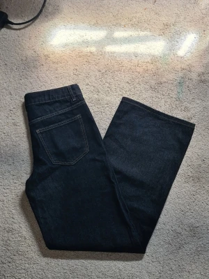 Mörkblå low wide jeans - Säljer ett par mörkblå jeans med vida ben och klassisk femficksdesign. Jeansen har kontrastsömmar och låg midja. Perfekta för dig som gillar en enkel och stilren look. Materialet är kraftig denim i bomull. Så himla fina och passar till allt! Prislapp finns kvar