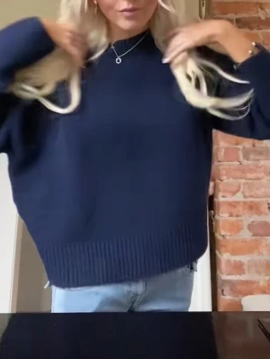 Blå stickad tröja från ZARA - En enkel och stilren mörkblå stickad tröja med rund halsringning och långa ärmar. Tröjan har ribbade muddar vid ärmslut och nederkant, vilket ger en snygg och avslappnad look. Perfekt att matcha med jeans för en casual stil.